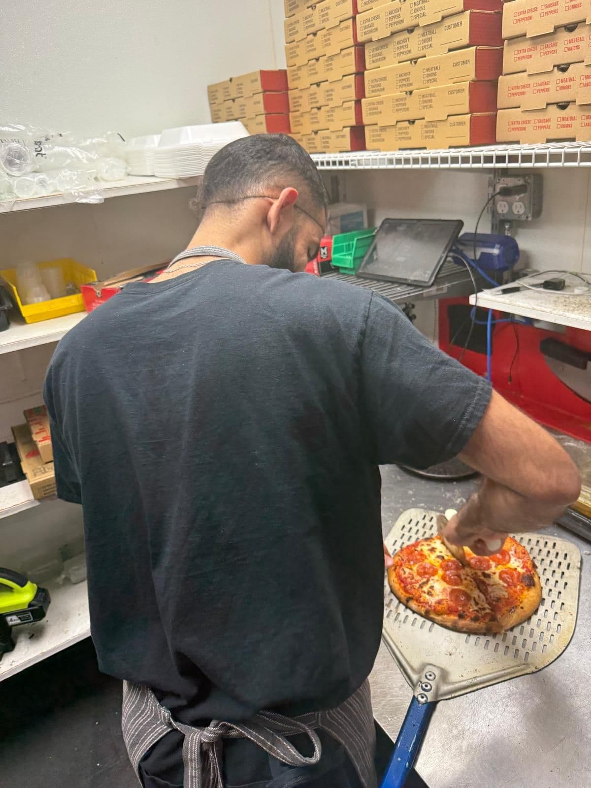 César trabajando en una cocina, con delantal, preparando una pizza